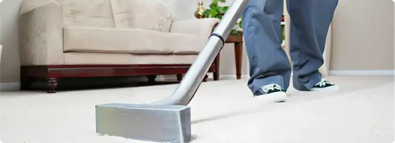 Carpet cleaning technician using a hot-water extraction wand on a light-colored carpet in a living room, Bloomington, IN.