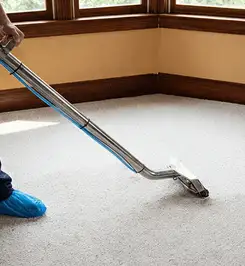 Steam carpet cleaning technician using a hot-water extraction wand on a residential carpet, wearing blue protective shoe covers Bloomington, IN.