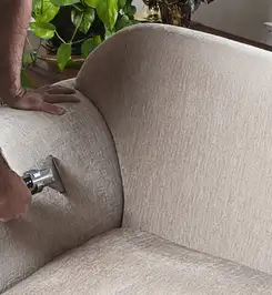 Professional upholstery cleaner deep-cleaning a fabric sofa with a handheld extraction tool and hose Bloomington, IN.