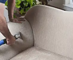 Professional upholstery cleaner deep-cleaning a fabric sofa with a handheld extraction tool and hose in Bloomington, IN.